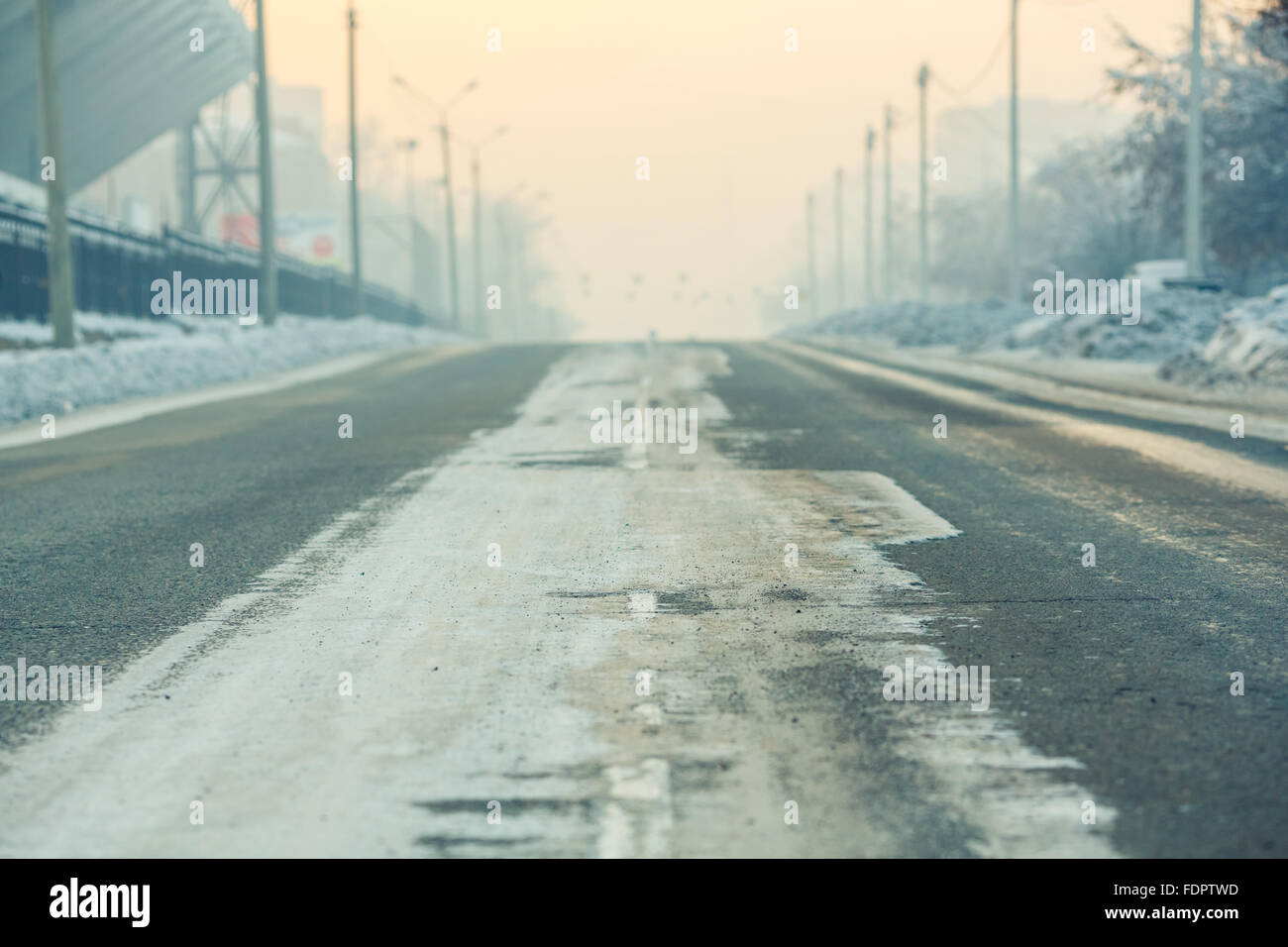 Los antecedentes, la carretera en una calle vacía en la ciudad, día de invierno frío, con nieve y reactivos al atardecer, la perspectiva aérea. Postes de luz a lo largo de los bordes de la carretera. Foto de stock