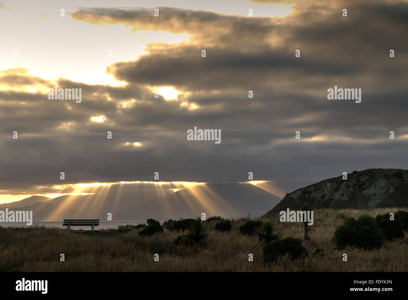 Un banco es silueteado sobre un promontorio por rayos crepusculares (rayos de sol o Dios vigas) como nubes de tormenta vuelco cabecero de Kaikoura. Foto de stock