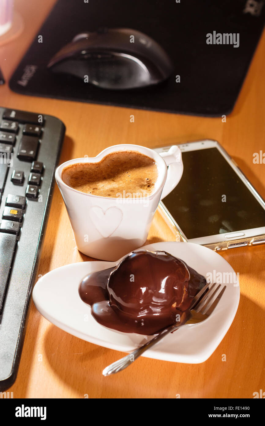 Taza de café y pastel de chocolate en forma de corazón junto a la placa del  teclado de la computadora portátil y el smartphone. Escritorio de oficina  Fotografía de stock - Alamy