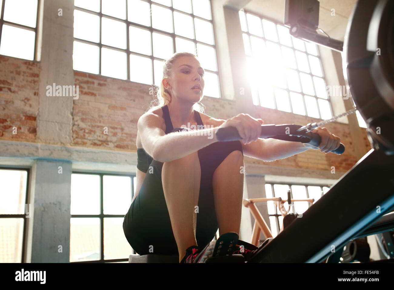 Mujer joven con máquina de remo en el gimnasio. Mujeres caucásicas haciendo ejercicios de cardio fitness club. Foto de stock