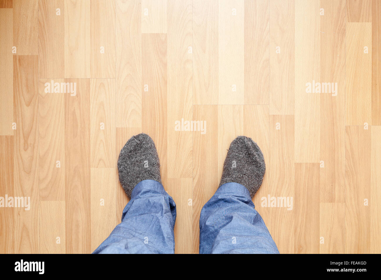 Pies masculinos en azul, pantalones largos y calcetines de lana gris de pie en el piso de madera Foto de stock