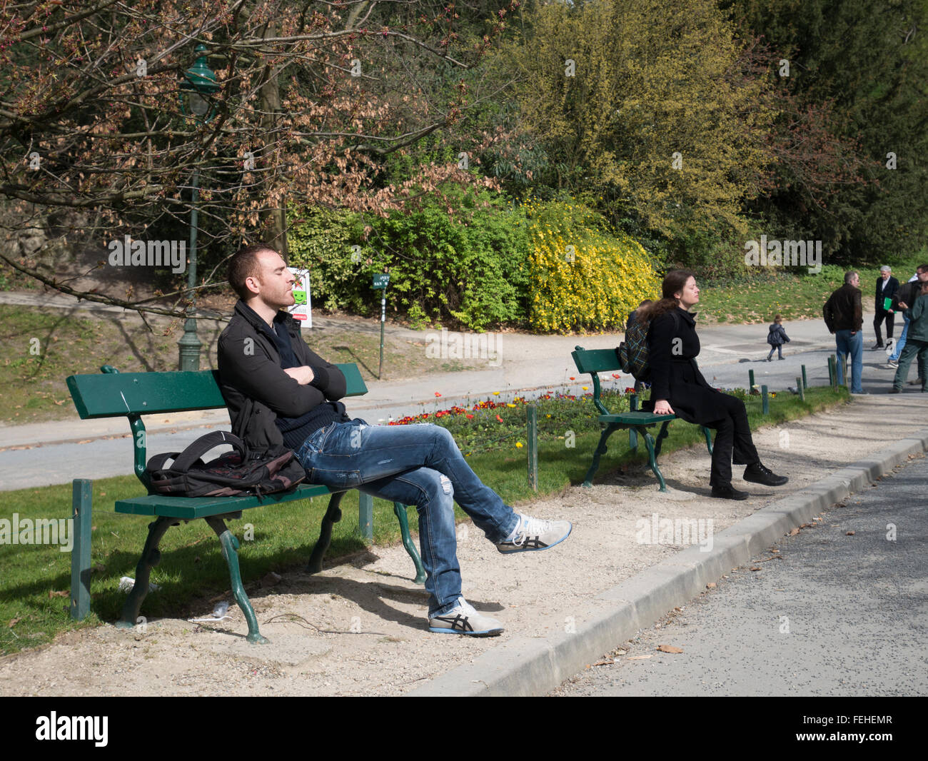 La gente en un parque sentarse en los bancos tomando el cálido sol Foto de stock