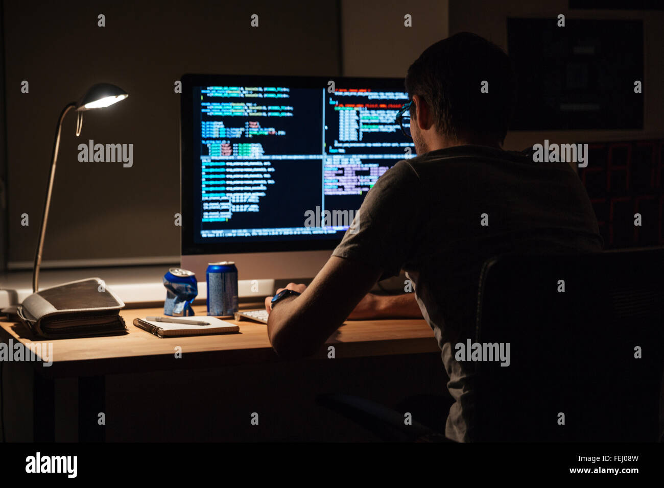 Vista posterior del programador moderno sentado y escribiendo código en una habitación oscura Foto de stock