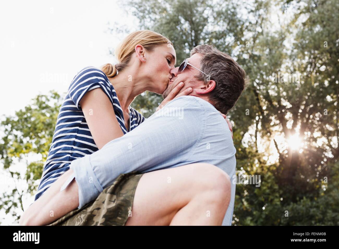 Ángulo de visión baja de pareja compartiendo apasionado beso en el parque Foto de stock