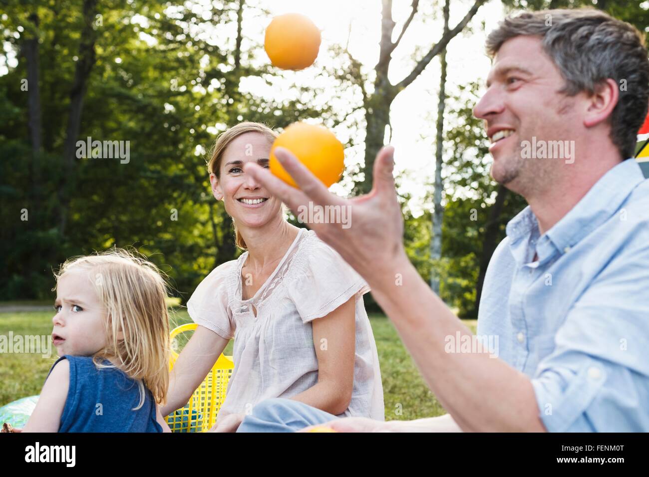 Hombre maduro malabarismos con naranjas al picnic familiar en el parque Foto de stock