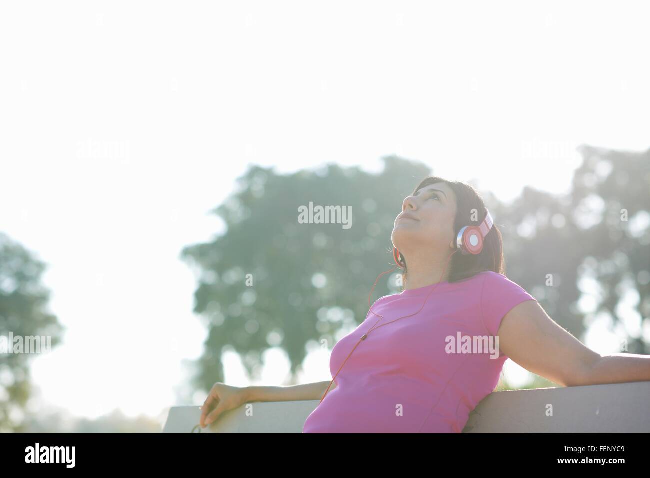Mujer madura, sentado en un banco del parque con los auriculares puestos mirando hacia arriba Foto de stock