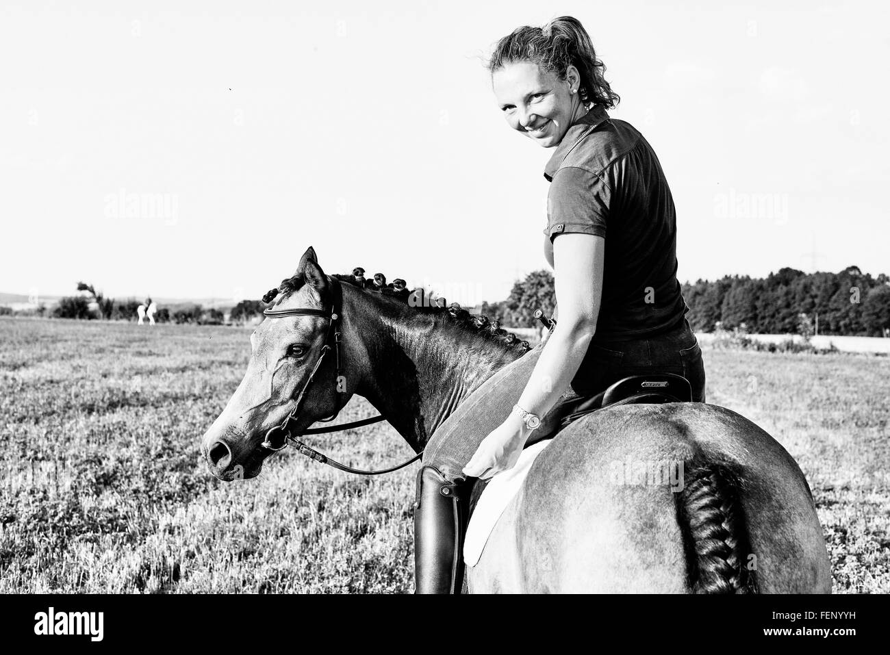 B&W retrato de mujer que monta a caballo en campo y mirando por encima del hombro Foto de stock