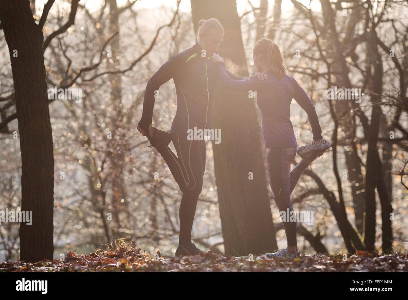 Pareja en bosque inclinada contra cada otra pierna levantada la celebración de estiramiento de pie Foto de stock