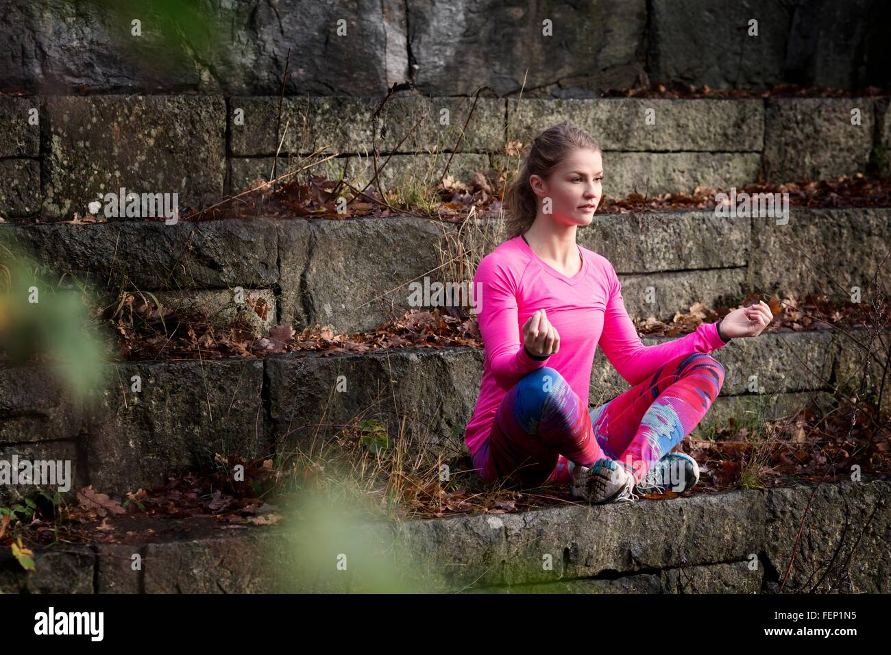 Mujer joven sentada piernas cruzadas en escalones de piedra meditando mirando lejos Foto de stock