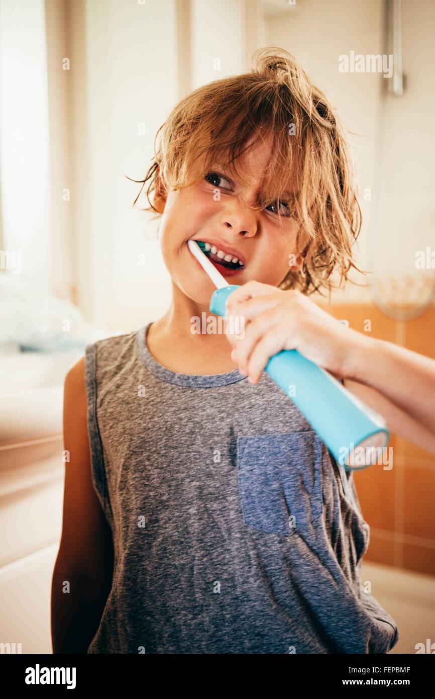 Chico con cepillo eléctrico para el cepillado de dientes, tirando rostro  Fotografía de stock - Alamy