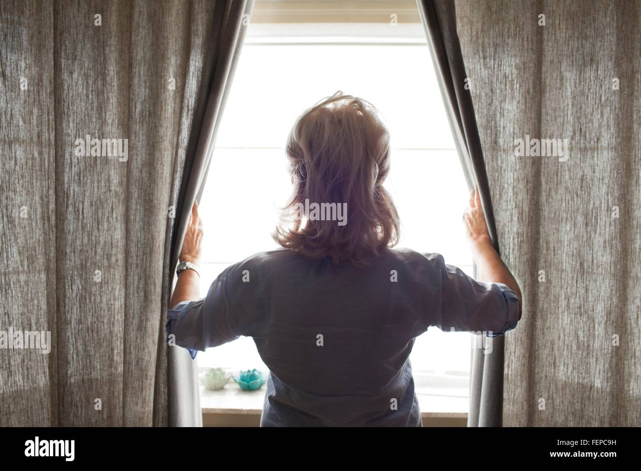 Mujer mayor apertura de cortinas, vista trasera Foto de stock