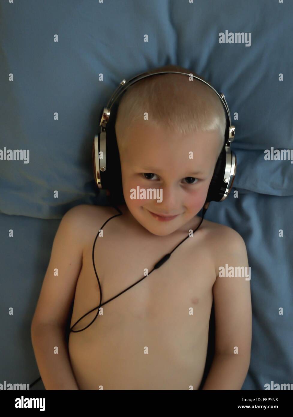 Ángulo alto retrato de descamisados sonriente niño usando auriculares en la cama Foto de stock