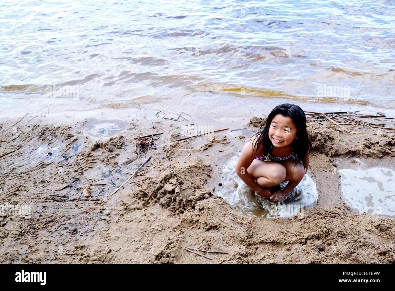 Un alto ángulo de vista de niña alegre en cuclillas en la playa Foto de stock