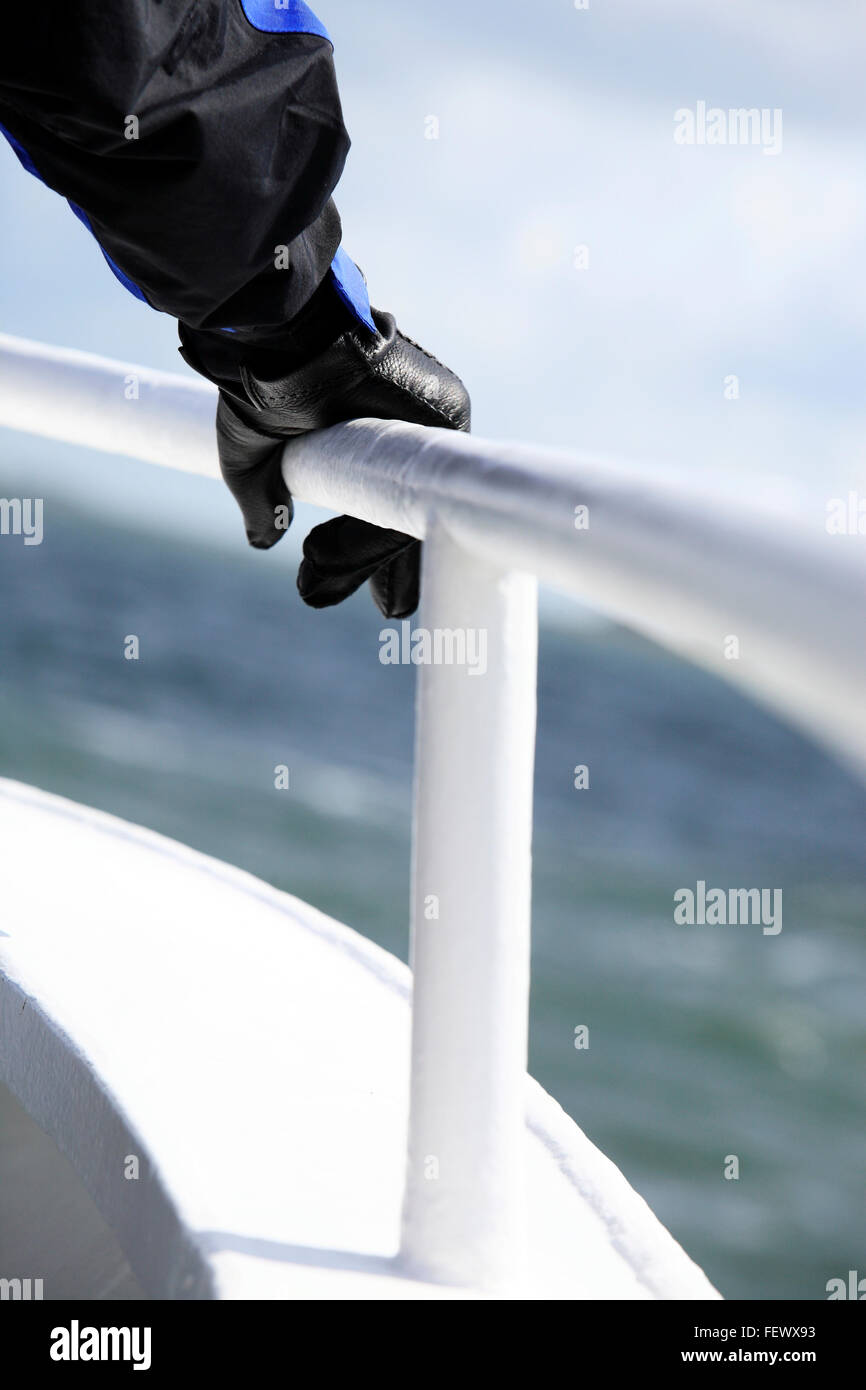 Mano llevaba un guante de cuero negro sujetando una barandilla blanca en un barco Foto de stock