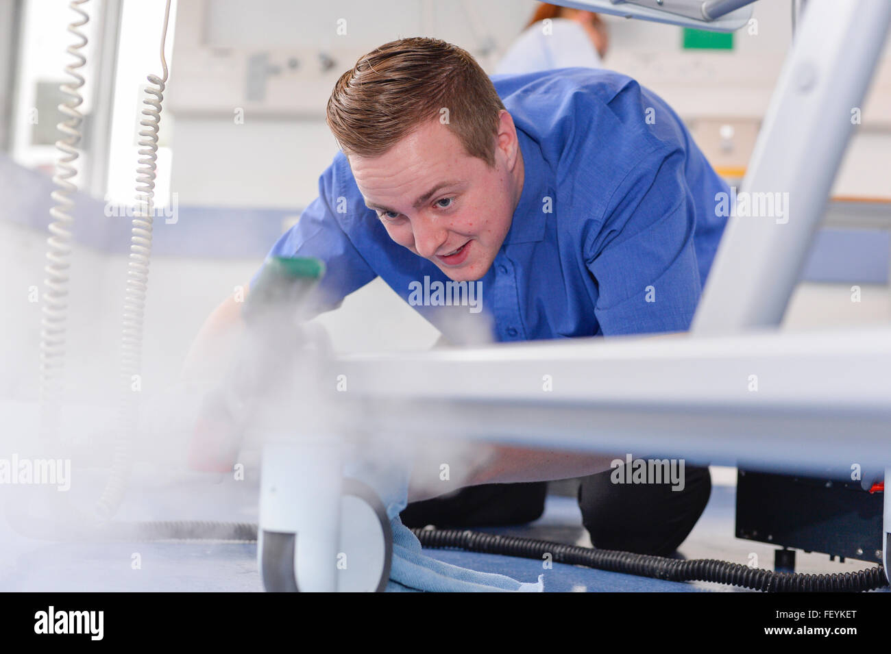 Un equipo de limpieza profesional matorrales, spray y limpie todas las superficies en salas de hospital. Crédito: Euan Cherry Foto de stock