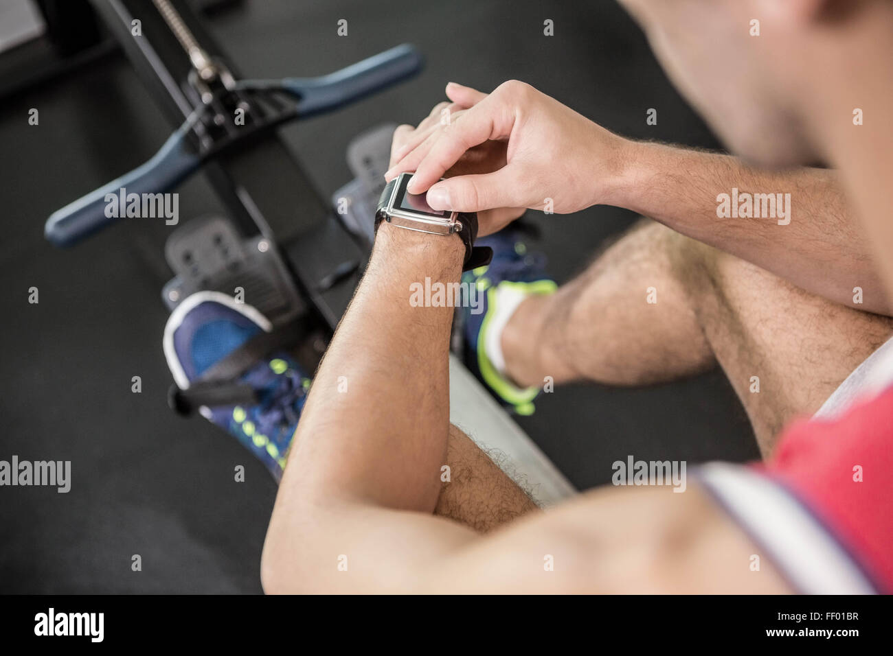 El hombre muscular en máquina de remo utilizando Smart Watch Foto de stock