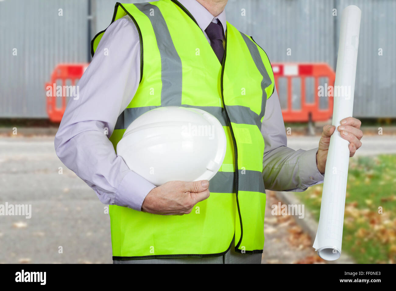 Ingeniero agrimensor en un chaleco de alta visibilidad amarillo la  celebración de dibujos y sombrero duro delante de las barreras de seguridad  de un sitio en construcción Fotografía de stock - Alamy