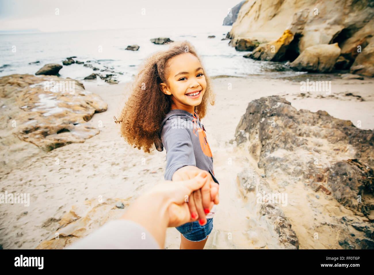 Chica tirando de la mano de la madre en la playa Foto de stock