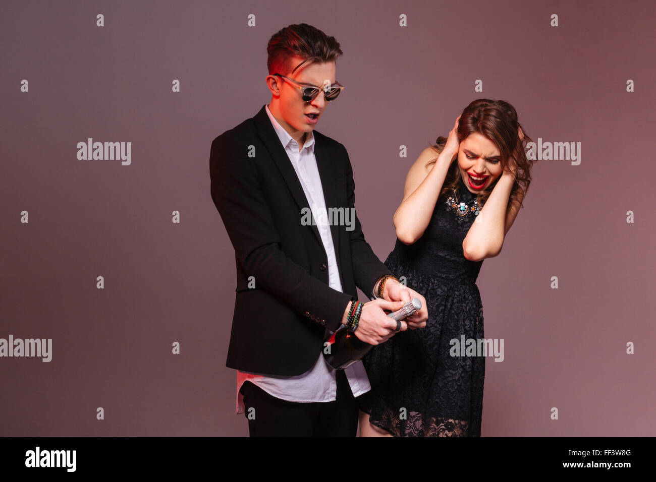 Feliz pareja joven de pie y abrir una botella de champaña sobre fondo púrpura Fotografía de stock - Alamy Feliz pareja joven de pie y abrir una botella de champaña sobre fondo púrpura Fotografía de stock - Alamy