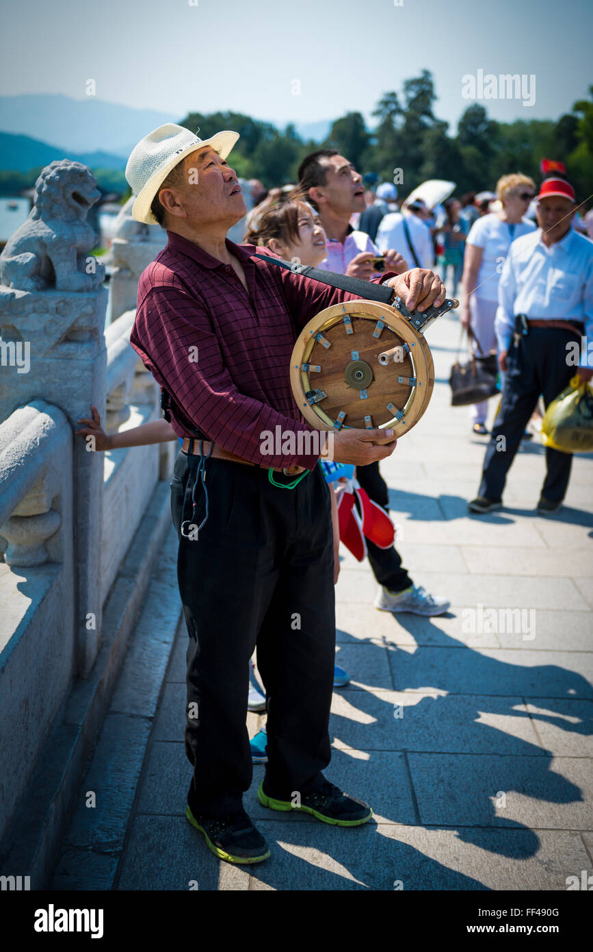 Hombre chino volar una cometa en el puente del palacio de verano, Beijing sunny buen humor con rueda artesanal, viendo a la gente pasar. Foto de stock