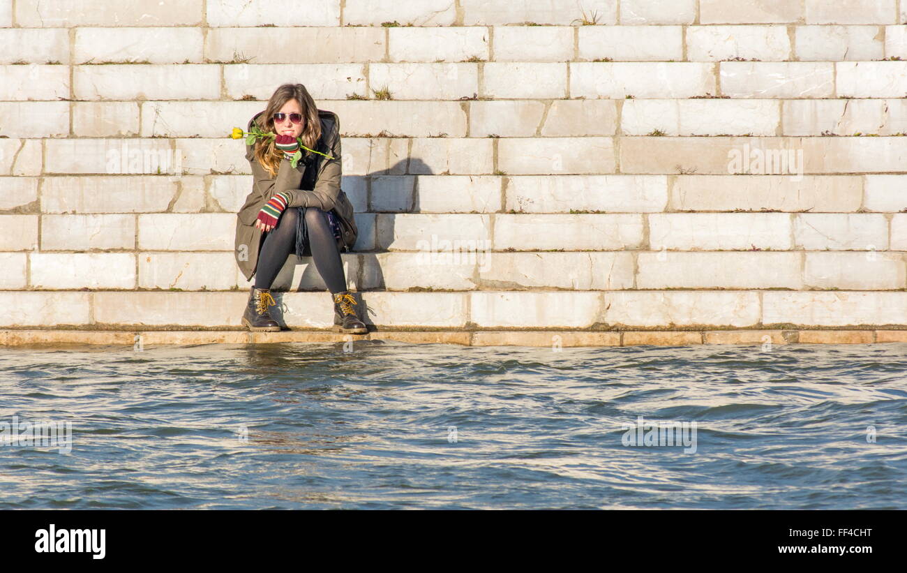 Chica sentada en la orilla del río al otro lado del río Foto de stock