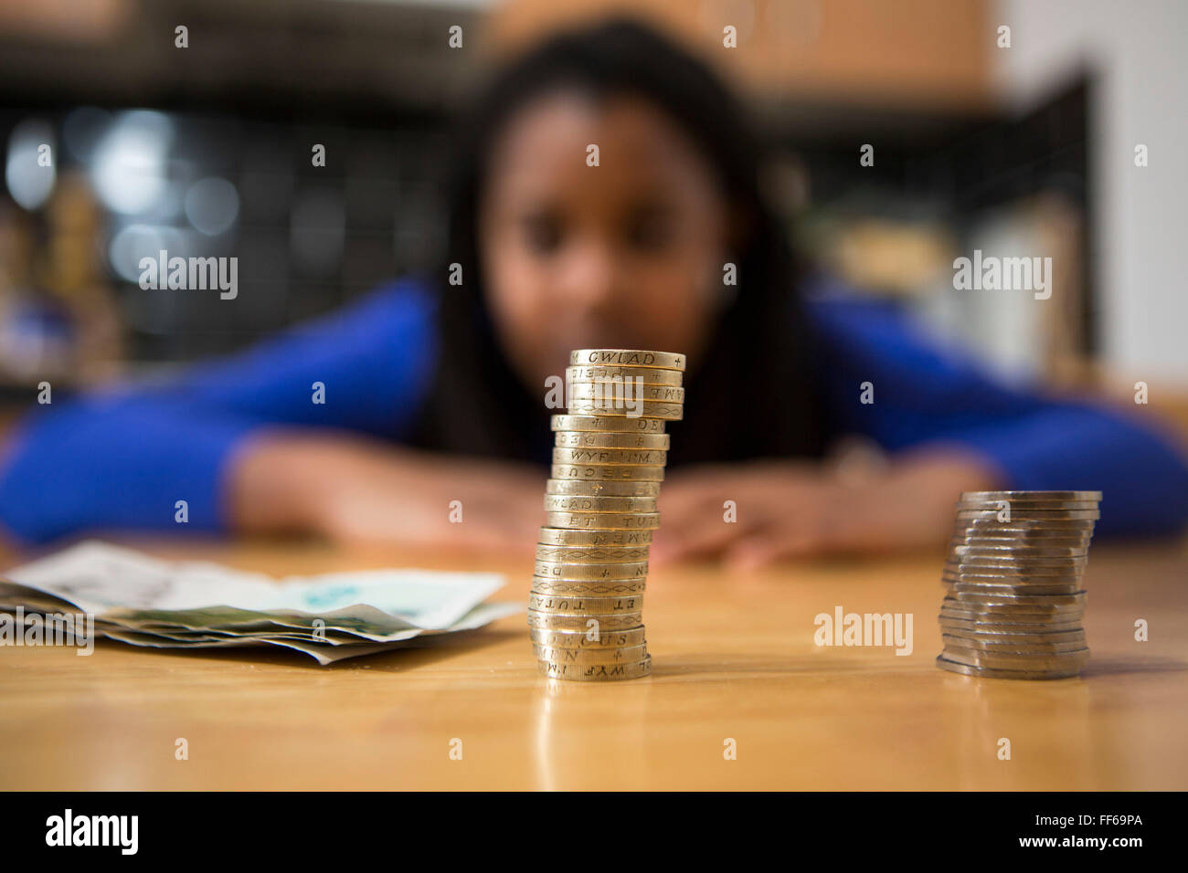 Una joven se sienta a la mesa de su cocina contando su dinero para pagar los recibos del hogar. Foto de stock