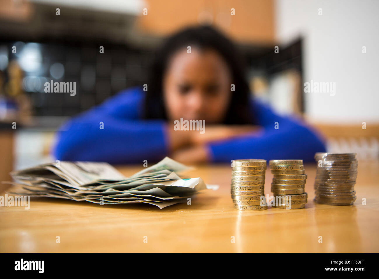 Una joven se sienta a la mesa de su cocina contando su dinero para pagar los recibos del hogar. Foto de stock