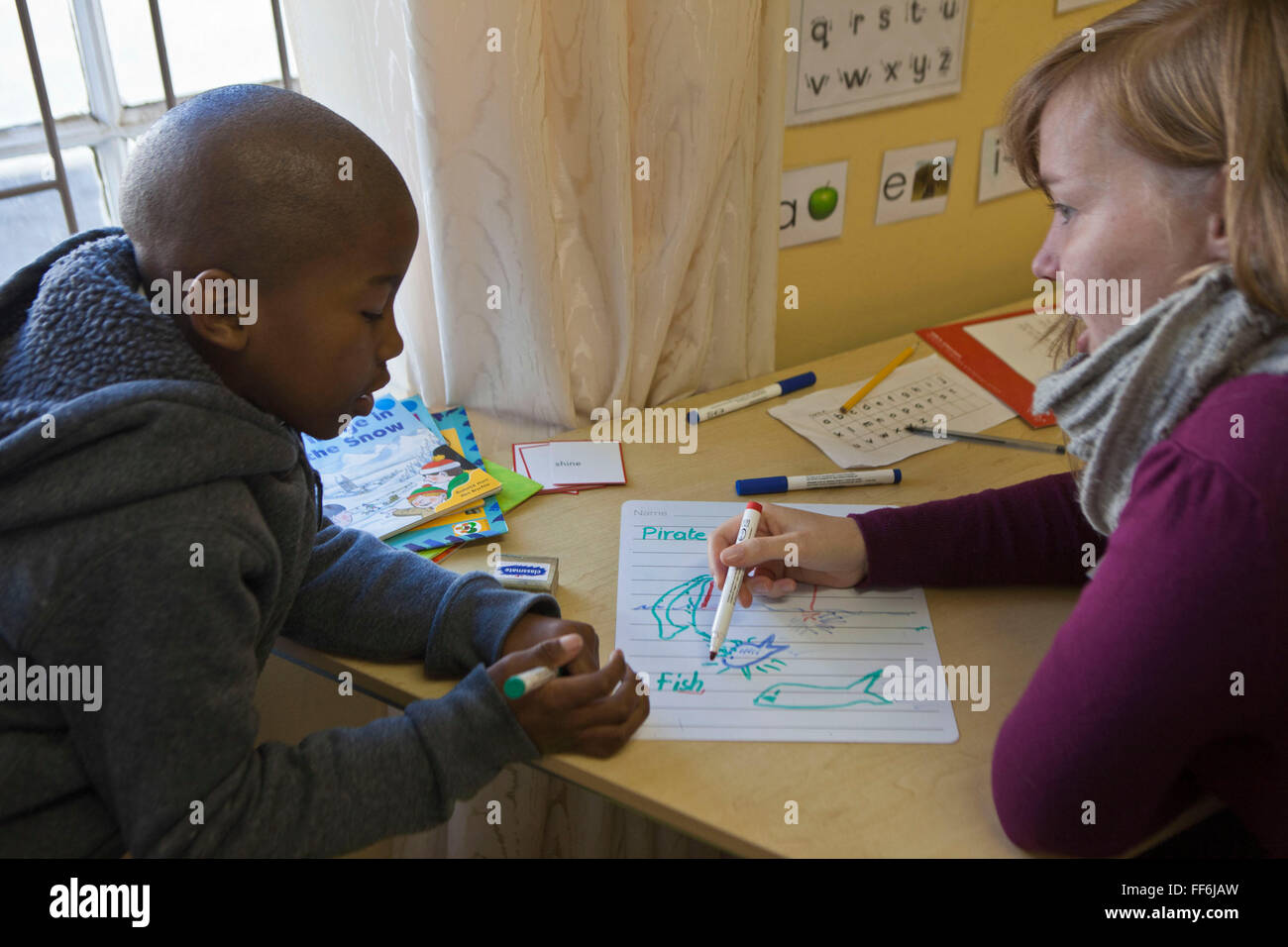 Un joven niño africano practica la escritura con una hembra de voluntario  en un aula en la escuela Zonnebloem, Cape Town, Sudáfrica. El voluntario  utiliza una variedad de herramientas de alfabetización para