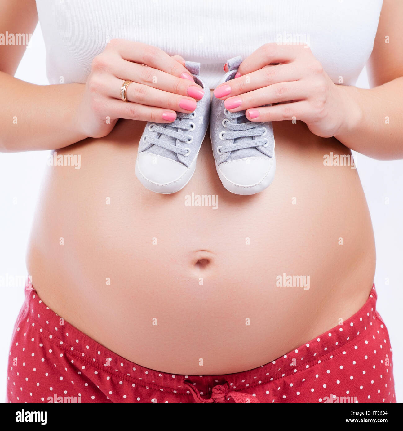 Pequeños zapatos para el feto en el vientre de la mujer embarazada Foto de stock