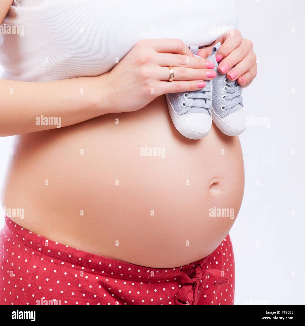 Pequeños zapatos para el feto en el vientre de la mujer embarazada Foto de stock