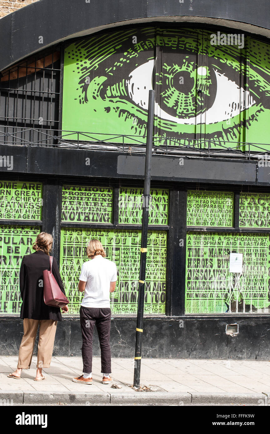 Dos jóvenes hipsters de pie delante de una pared decorada con un ojo grande y escritos. Foto de stock