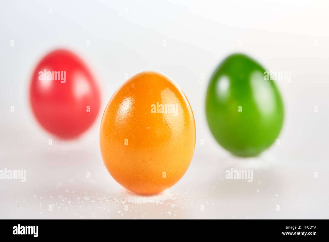 Tres huevos de pascua de color aislado de pie en pequeños montones de sal sobre fondo blanco. Foto de stock