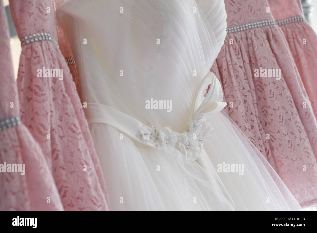 El tradicional vestido blanco colgado entre cuatro rosa vestidos de damas de honor Foto de stock