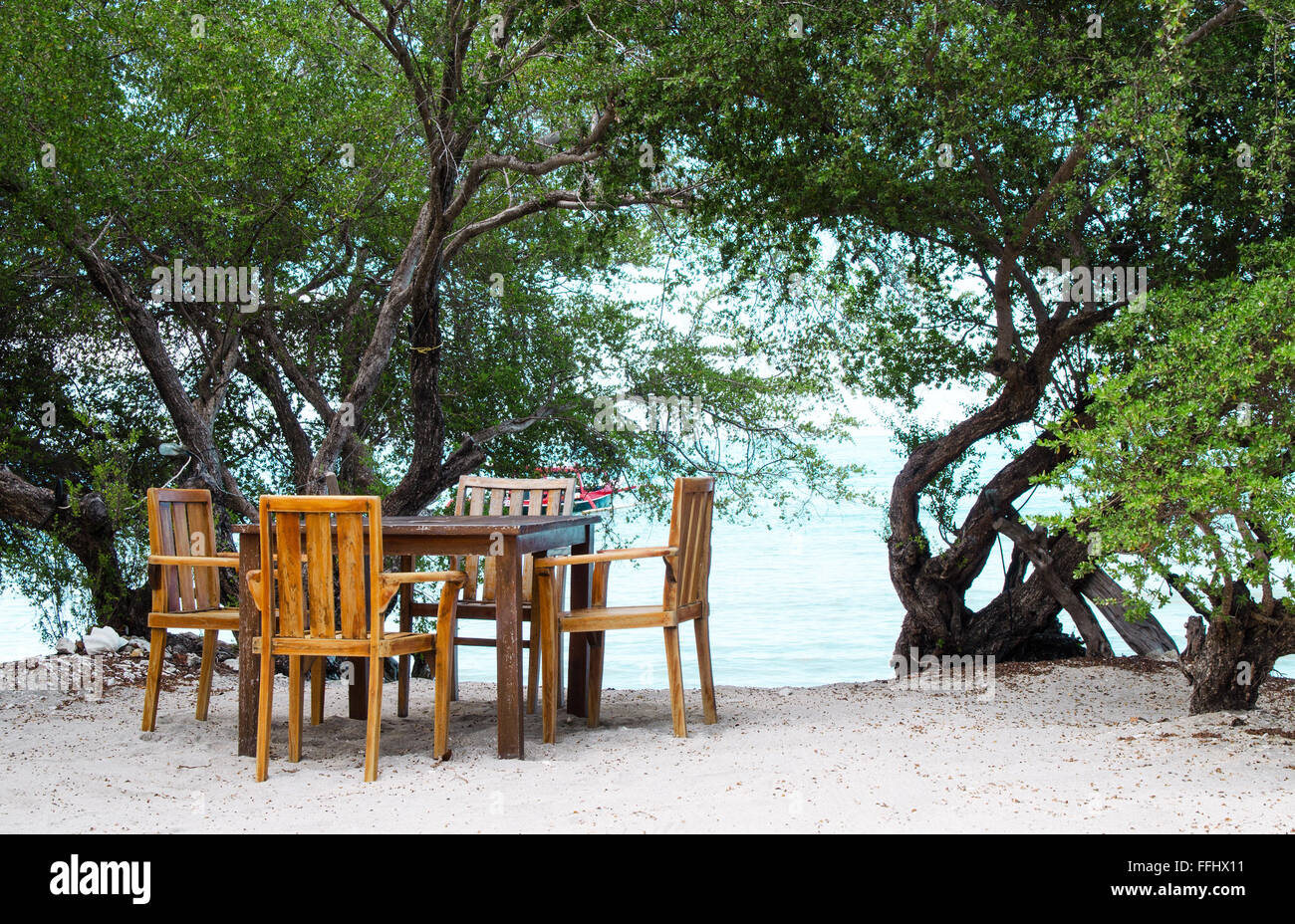 Lugar romántico con una mesa en la playa bajo la sombra de los árboles. Imágenes de stock. Foto de stock