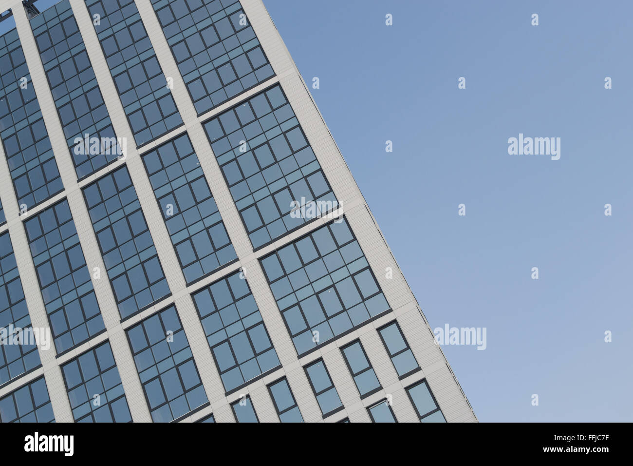 Moderno edificio de gran altura con ángulos agudos mostrando reflejos de un cielo azul brillante. Nadie en la imagen y Foto de stock