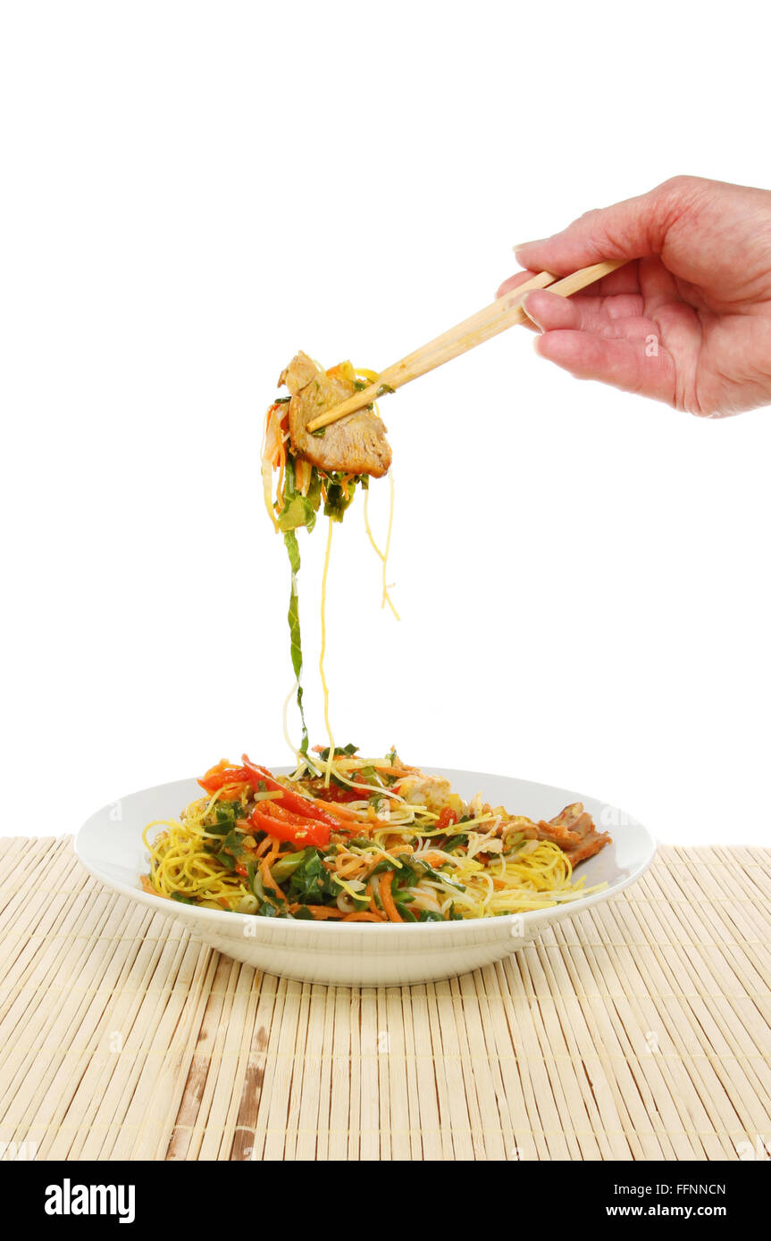 Mano sosteniendo los palillos con fideos de Singapur sobre un recipiente sobre un fondo blanco. Foto de stock