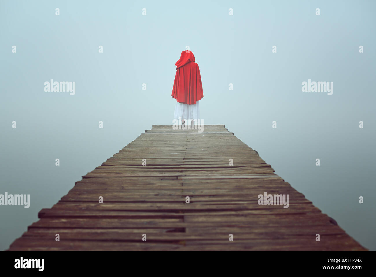 Capucha roja mujer mira al lago brumoso en un muelle de madera . La tristeza y la soledad concepto Foto de stock