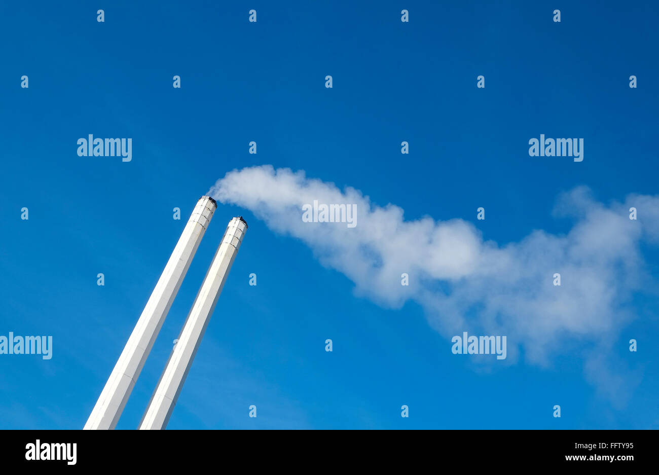 Dos chimeneas de fábrica, humo blanco y azul del cielo Foto de stock