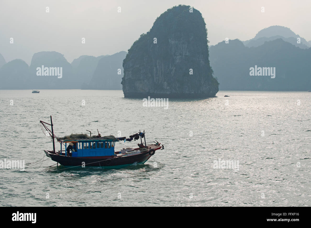 Un pequeño barco pesquero el automovilismo en un mar en calma en la Bahía de Halong con misty karsts de piedra caliza detrás de Vietnam Foto de stock