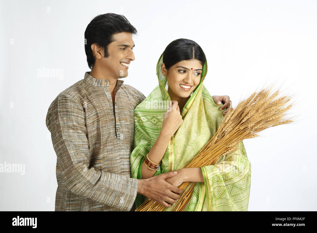 El agricultor indio mirando esposa celebración recolectado la cosecha de trigo de oro - MR#743A, 743B Foto de stock