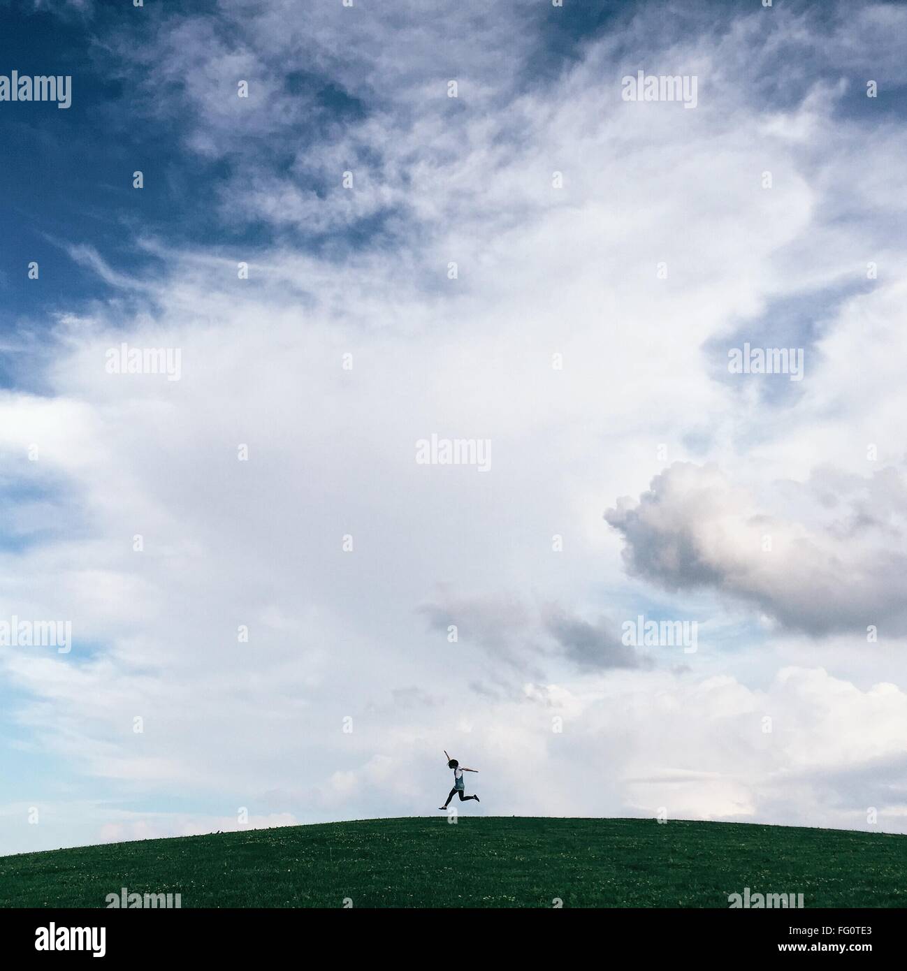 Ángulo de visión baja de persona saltando en grassy hill contra el cielo nublado Foto de stock