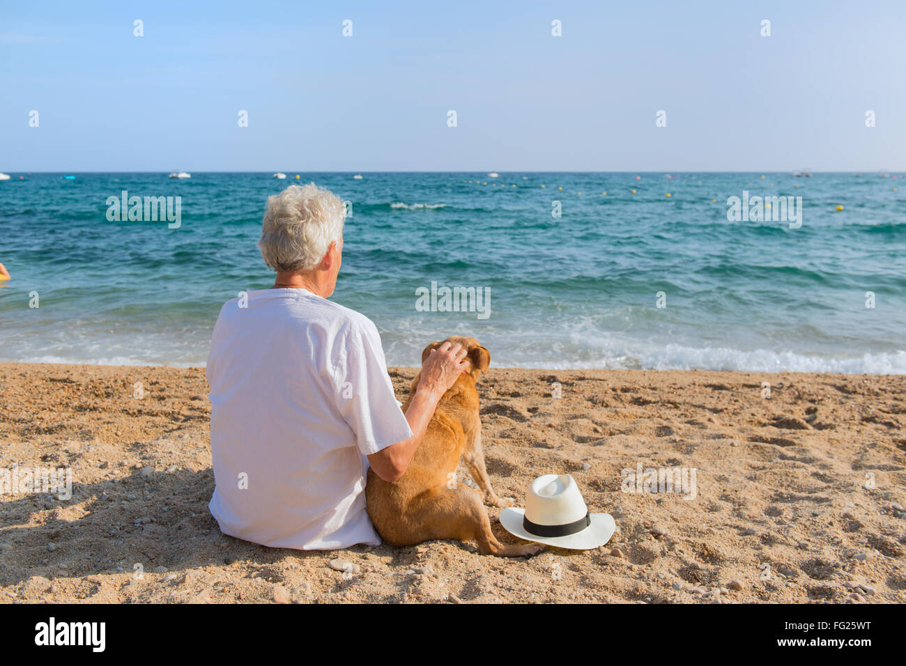Altos hombre con perro en traje blanco sentado en la playa. Foto de stock