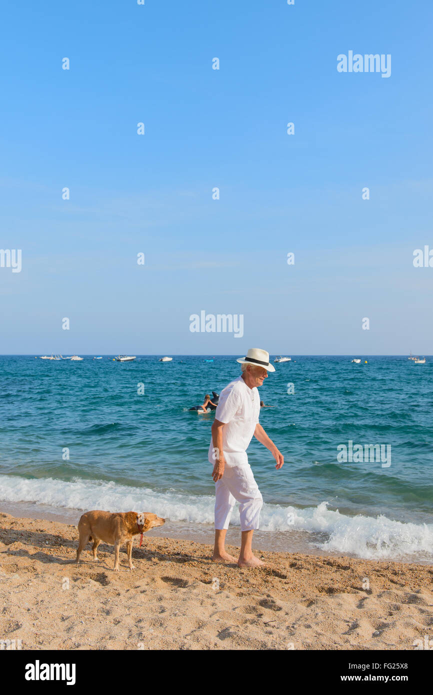 Altos hombre con traje blanco perro a caminar en la playa. Foto de stock