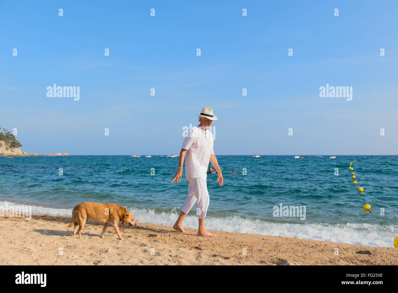 Altos hombre con traje blanco perro a caminar en la playa. Foto de stock