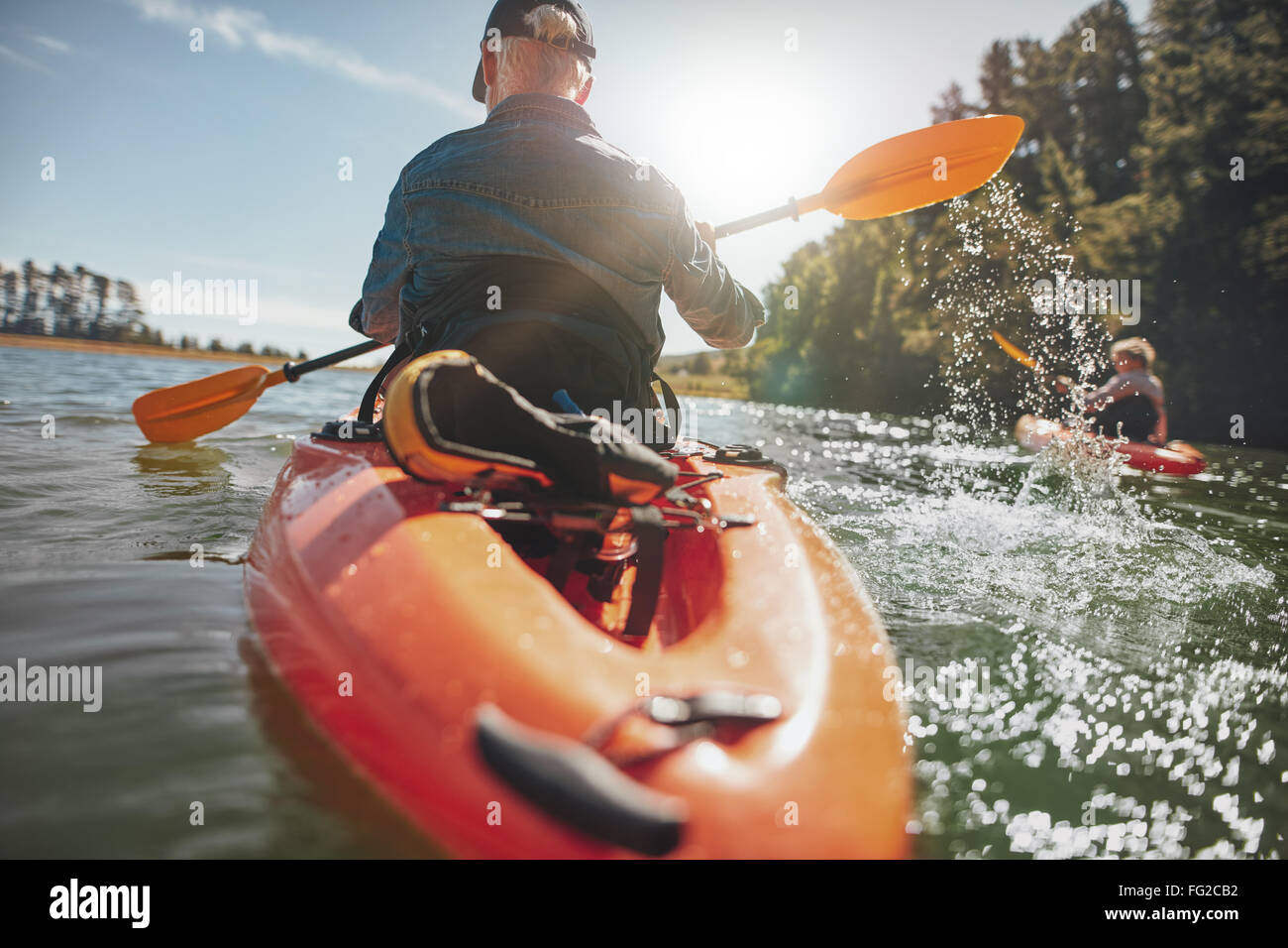 Vista trasera del hombre remando kayak en el lago con la mujer en el fondo. Par hacer kayak en el lago en un día soleado. Foto de stock