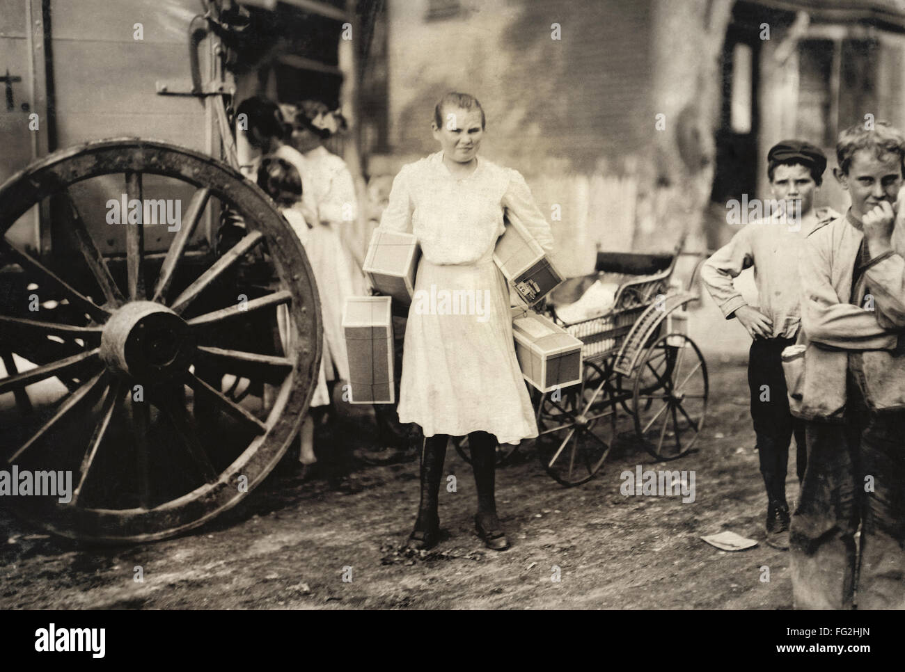 HINE: Inicio Industria, 1912. /NA NIÑA cargando varias cajas de etiquetas de prendas de vestir en la calle Roxbury, Massachusetts. Fotografía por Lewis Wickes Hine, agosto de 1912. Foto de stock