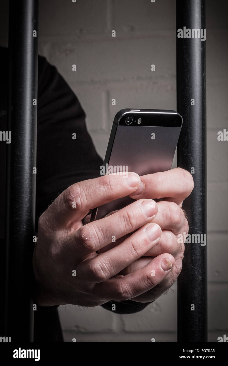 Un preso en la prisión a través de un teléfono móvil tras las rejas en una celda Foto de stock