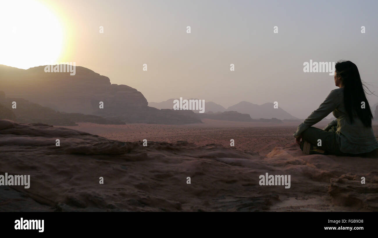 Mujer meditando en el desierto contra el cielo durante el amanecer Foto de stock