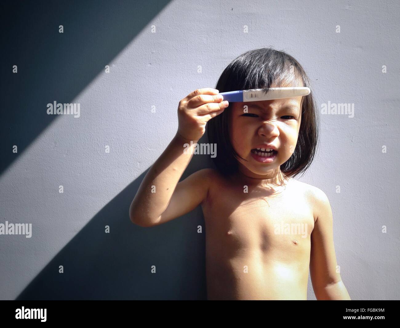 Retrato de Topless Chica sujetando test de embarazo mientras está de pie contra la pared Foto de stock