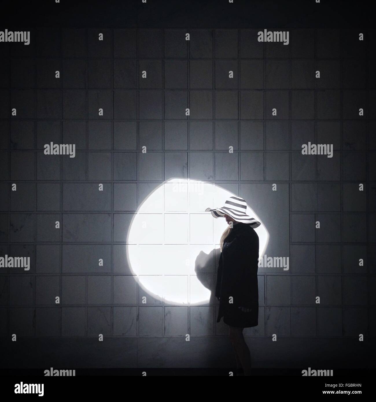Mujer vistiendo sombrero contra la luz solar en la pared de mosaico Foto de stock
